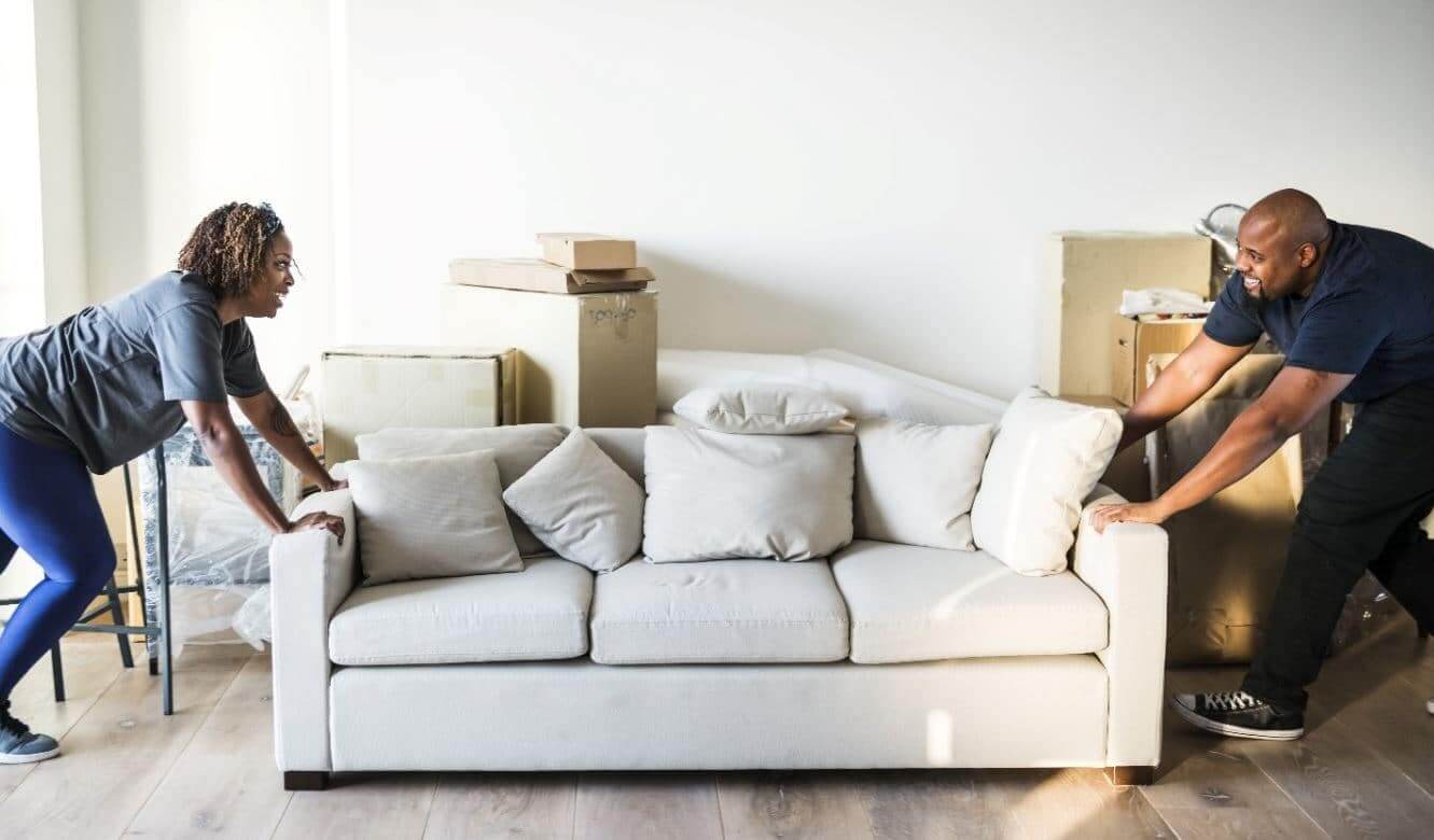 Couple moving white couch in apartment