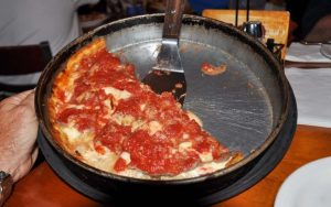 Pequod's Pizza in a pan with a hand holding it