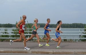 four people running in marathon along a lake